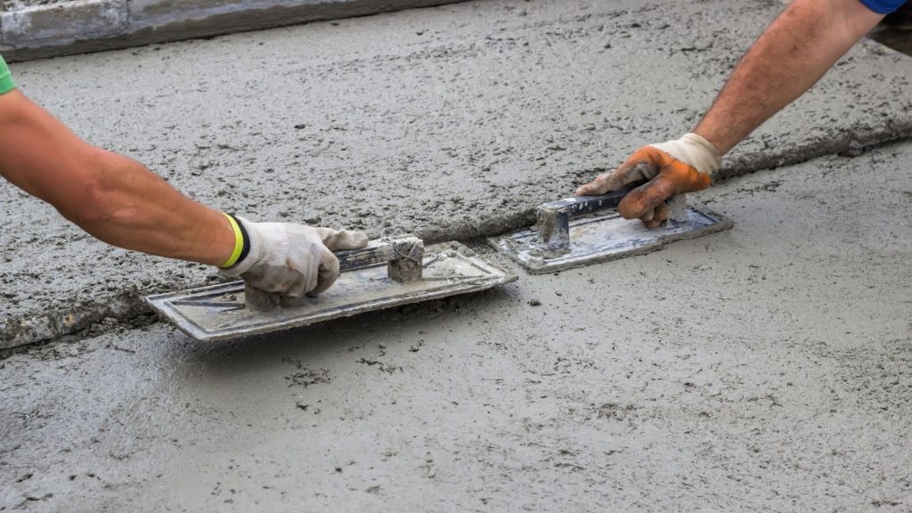 Two tradespeople hand-finishing a freshly poured concrete slab with trowels
