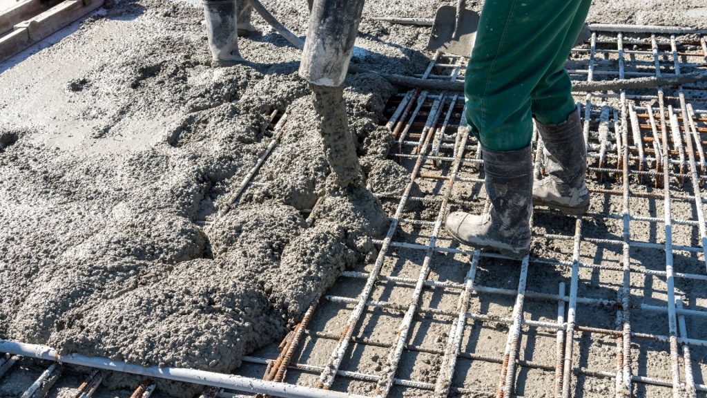 Worker placing wet concrete over steel reinforcement mesh on a construction site
