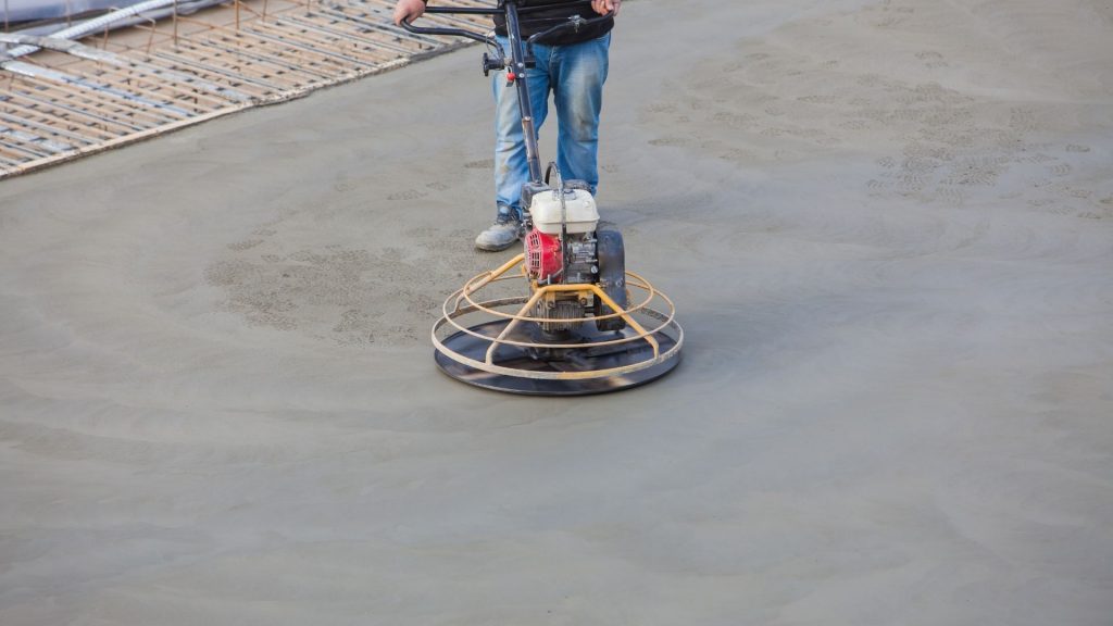 Worker in blue overalls operating a concrete floor grinder