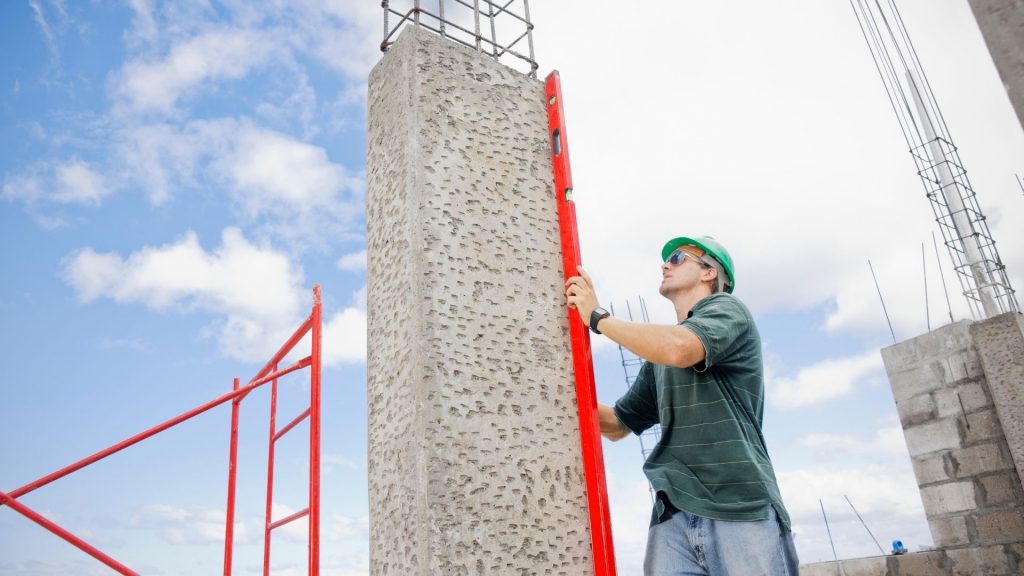 Construction worker checking a concrete column for level with a spirit level on site