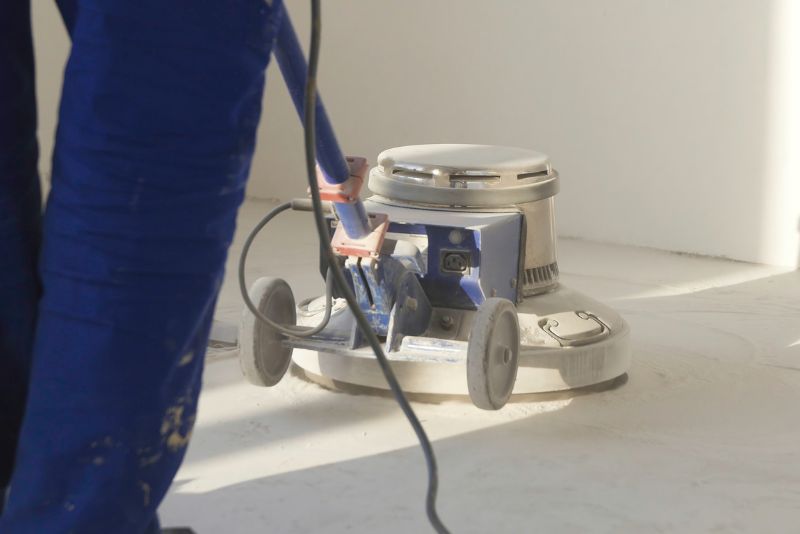 Worker in blue overalls operating a concrete floor grinder