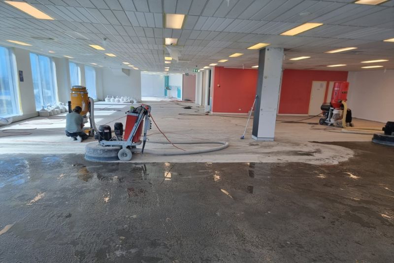 Worker grinding a concrete floor in a large commercial fit-out with dust extraction equipment